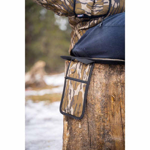 Person sitting on a Mobile Warming camouflage heated seat cushion on a tree stump