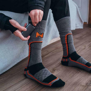 Person inserting a Mobile Warming battery pack into the pocket of a grey and black heated sock