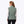 Back view of a woman wearing a sage green Mobile Warming quilted vest over a white long sleeve shirt