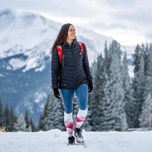 Woman wearing a black Mobile Warming heated jacket and red backpack walking in a snowy mountain landscape