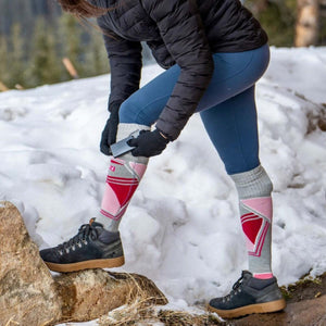 Person inserting a Mobile Warming battery pack into a heated sock in a snowy outdoor setting