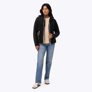 Woman wearing a black Mobile Warming fleece jacket with white zipper details over a cream sweater and blue jeans