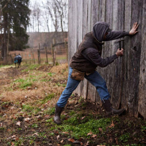 Person wearing Muck boots hammering a wooden wall on a farm