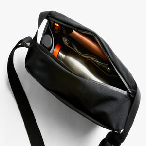 Open Bellroy black sling bag containing a water bottle and personal items