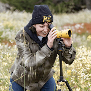 Person using NOCS Provisions yellow spotting scope on a tripod in a field of wildflowers