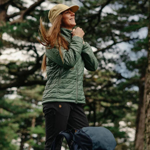 Woman wearing a green FjallRaven quilted jacket and tan cap outdoors