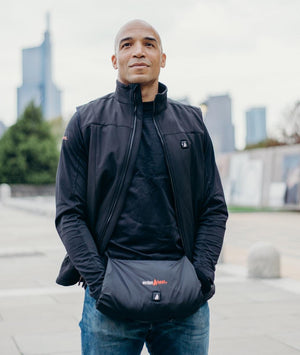 Man wearing a black ActionHeat heated vest with a hand warmer pouch in front of a city skyline