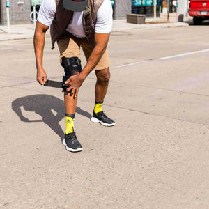 Person adjusting a black Onyx knee brace on their leg while standing outdoors