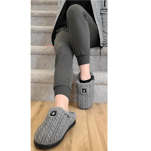 Person wearing grey cable knit ActionHeat slippers while sitting on carpeted stairs
