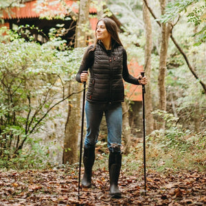 Woman wearing ActionHeat black puffer vest and hiking with poles in a wooded area