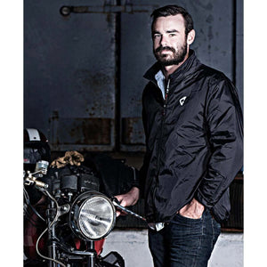 Man with beard wearing a black windbreaker jacket standing next to a motorcycle