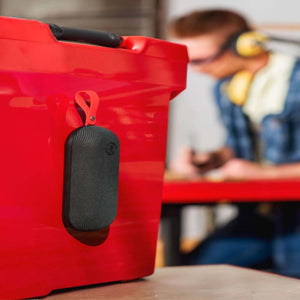 Outdoor Tech black portable speaker hanging from a red storage bin