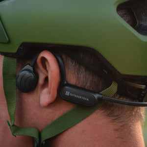 Outdoor Tech bone conduction headphones worn under a green helmet