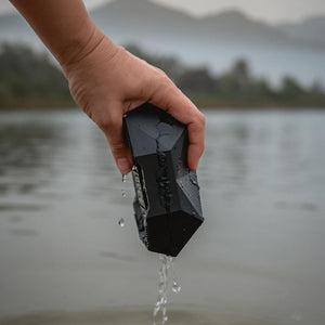 Hand holding a wet Outdoor Tech portable speaker over water