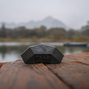 Outdoor Tech black geometric portable speaker on a wooden dock by a lake
