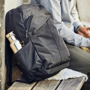 Black backpack with a metal water bottle in the side pocket resting on a wooden bench
