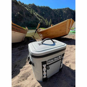 Polar Bear soft cooler on a sandy riverbank with wooden boats in the background