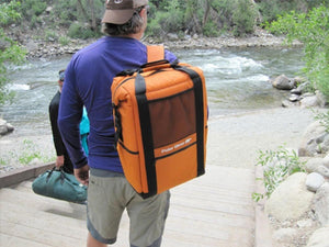 Person wearing an orange Polar Bear Coolers backpack cooler while walking down wooden steps near a river