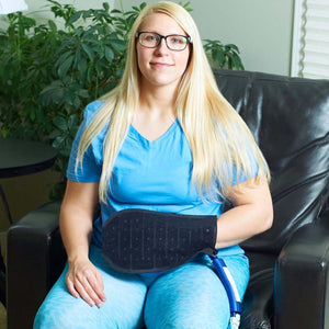 Woman wearing a Polar Products black therapy wrap on her hand while sitting in a chair