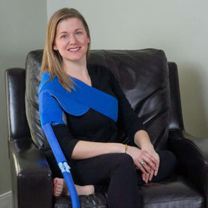 Woman wearing a blue Polar Products shoulder ice pack wrap while sitting in a leather chair