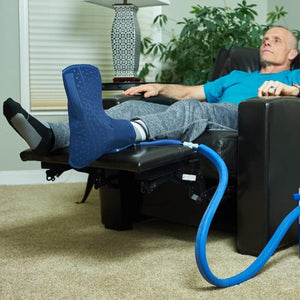 Man resting in a recliner with a blue cold therapy foot wrap connected to a cooling system