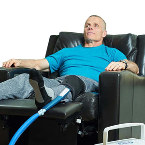 Man using a Polar Products knee cold therapy wrap connected to a cooling unit while sitting in a recliner