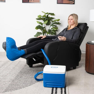 Woman using a Polar Products cold therapy foot wrap connected to a cooling unit while sitting in a recliner