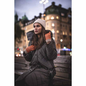Woman wearing Hestra tan leather gloves and a winter coat sitting on a bench