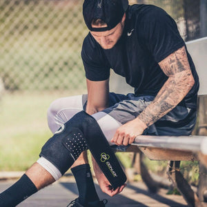 Athlete adjusting a black DonJoy knee brace while sitting on a bench