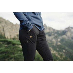 Person wearing black Fjallraven trousers with side zip pocket and blue jacket in mountain landscape