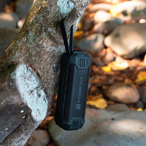 Outdoor Tech black portable speaker hanging from a tree branch