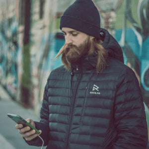 Man wearing a black Ravean puffer jacket and beanie looking at a smartphone