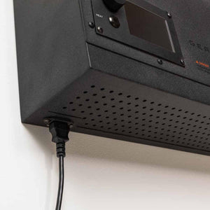 Black power cord plugged into the underside of a black electronic device with a perforated metal casing