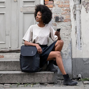 Woman sitting on stone steps holding a smartphone next to a black Thule backpack