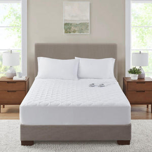 Serta white quilted heated mattress pad on a bed with two pillows