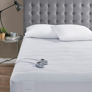 Serta white heated mattress pad with dual controllers on a bed with a grey tufted headboard