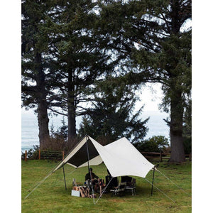 Snow Peak tarp set up over camping chairs and gear on a grassy lawn near the ocean