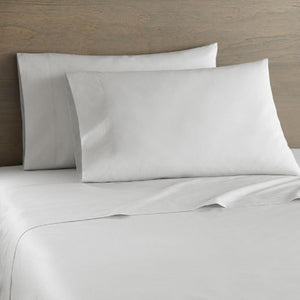 Shavel white bed sheet set with two pillows against a wooden headboard