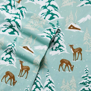 Shavel fabric with winter forest pattern featuring deer and cabins on light green background