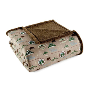 Folded tan throw blanket with brown sherpa lining and camping themed bear and mountain print