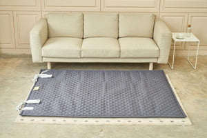 Grey quilted electric heating mat on a beige rug in front of a beige sofa