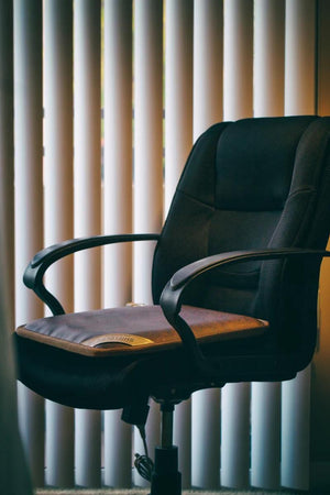 Shield Life heating pad placed on a black office chair in front of vertical blinds