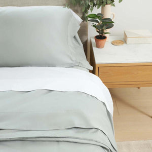 Sage green bedding set with white flat sheet on a wooden nightstand with a small plant