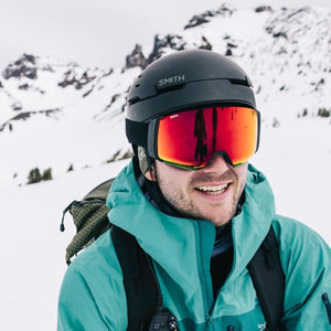 Person wearing a Smith Optics helmet and red mirrored goggles in a snowy mountain environment