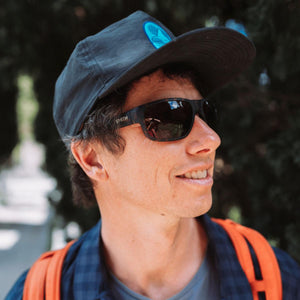 Person wearing Smith sunglasses and a baseball cap with an orange backpack