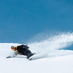 Snowboarder wearing Smith Optics goggles carving through snow