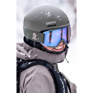 Person wearing a Smith Optics olive green ski helmet and blue mirrored goggles in the snow