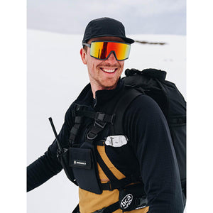 Person wearing a black cap, orange goggles, and a backpack in a snowy environment
