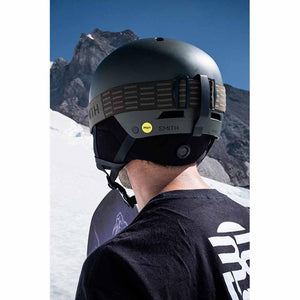 Back view of a person wearing a matte olive Smith Optics helmet with MIPS technology in a snowy mountain setting