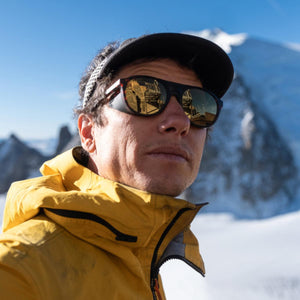 Person wearing Smith Optics sunglasses and a yellow jacket in a snowy mountain landscape